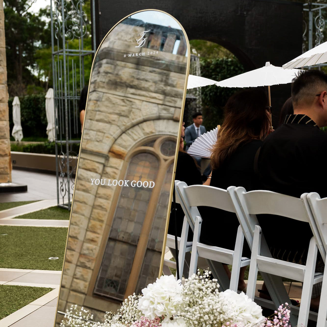 personalised decorative mirror with 'YOU LOOK GOOD' text at an outdoor event with white chairs and umbrellas.