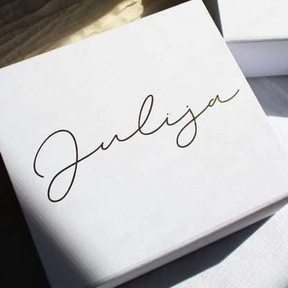A close-up of a white textured bridesmaid proposal gift box with the name 'Julija' written in elegant black cursive script, photographed in bright natural light.