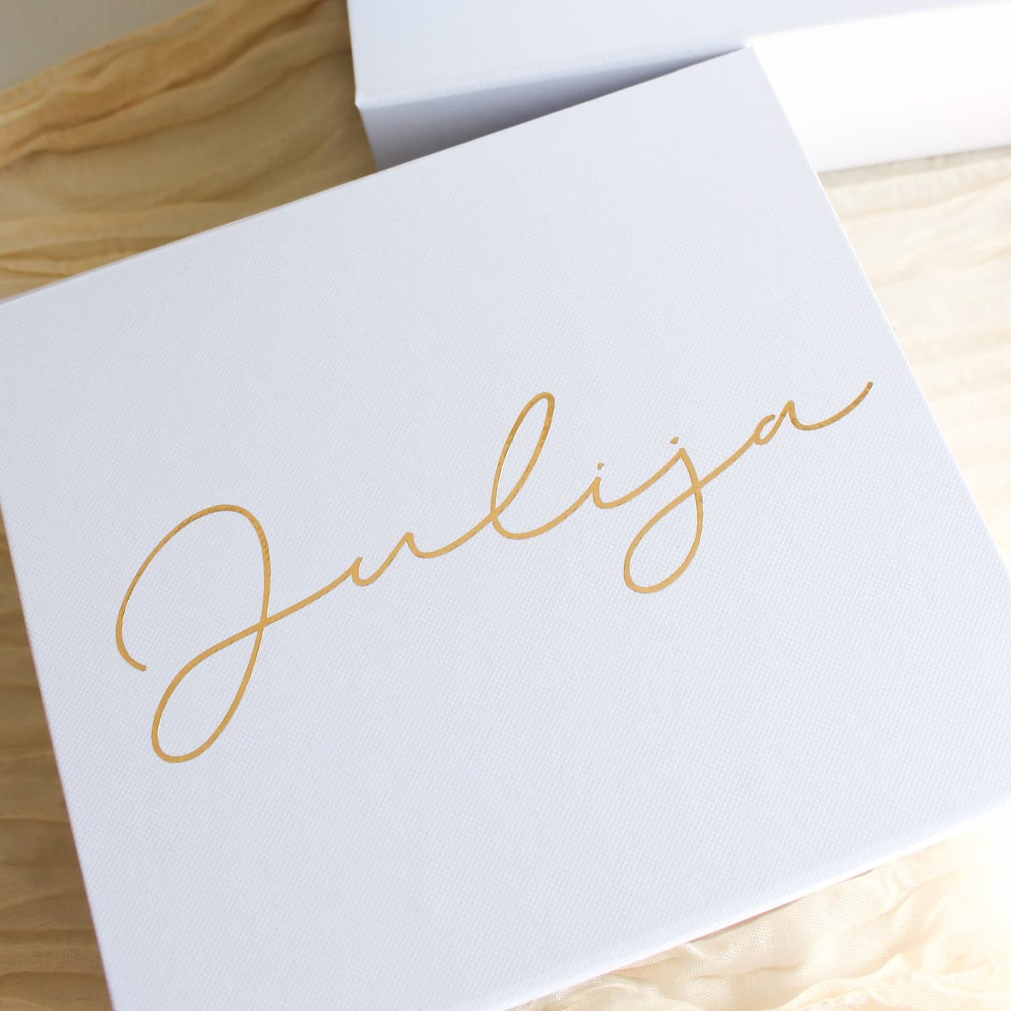 A white square bridesmaid proposal gift box with the name 'Julija' written in elegant gold cursive script, resting on a light wood surface.