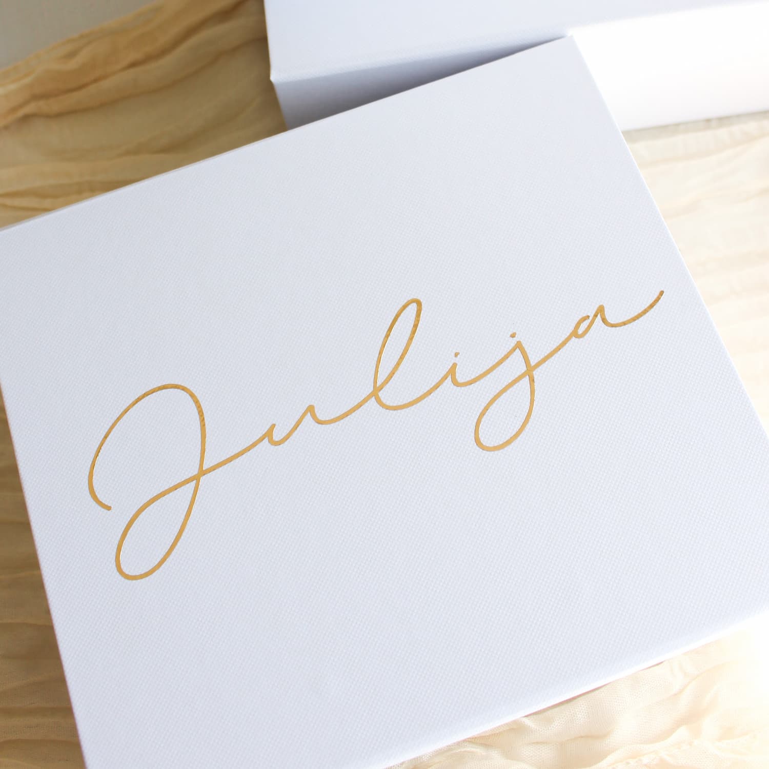 A white square bridesmaid proposal gift box with the name 'Julija' written in elegant gold cursive script, resting on a light wood surface.