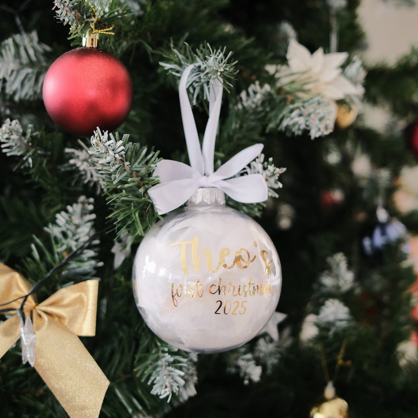Decorative Feather Christmas ornament with 'Theo's first Christmas 2025' text on a tree.