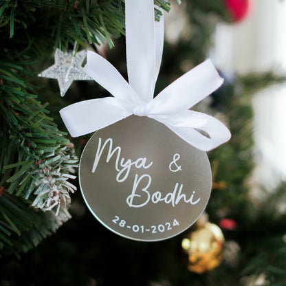 Decorative ornament with 'Mya & Bodhi' and a date, hanging on a Christmas tree.