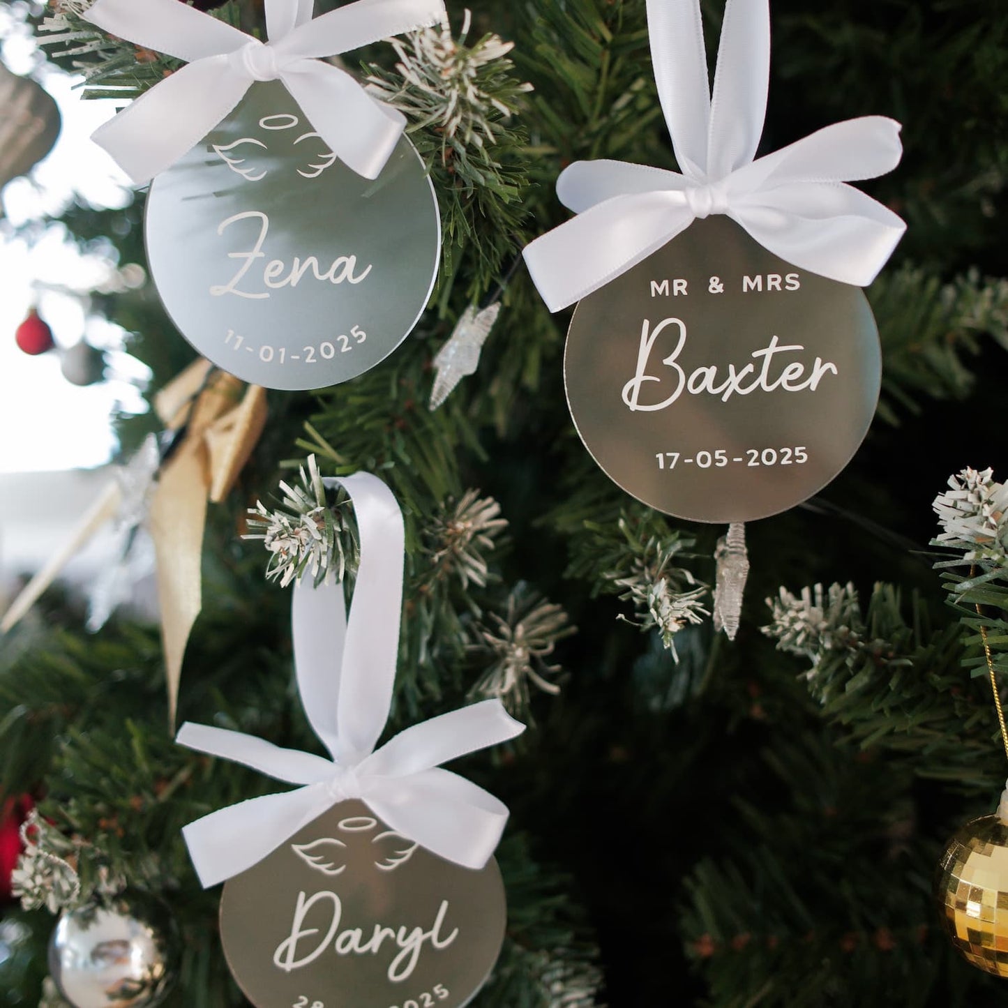 Personalized Christmas ornaments with names and dates hanging on a tree.