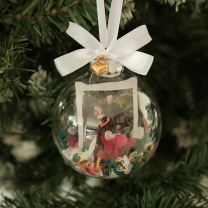 Decorative Christmas ornament with a couple's photo inside, tied with a white ribbon on a tree.