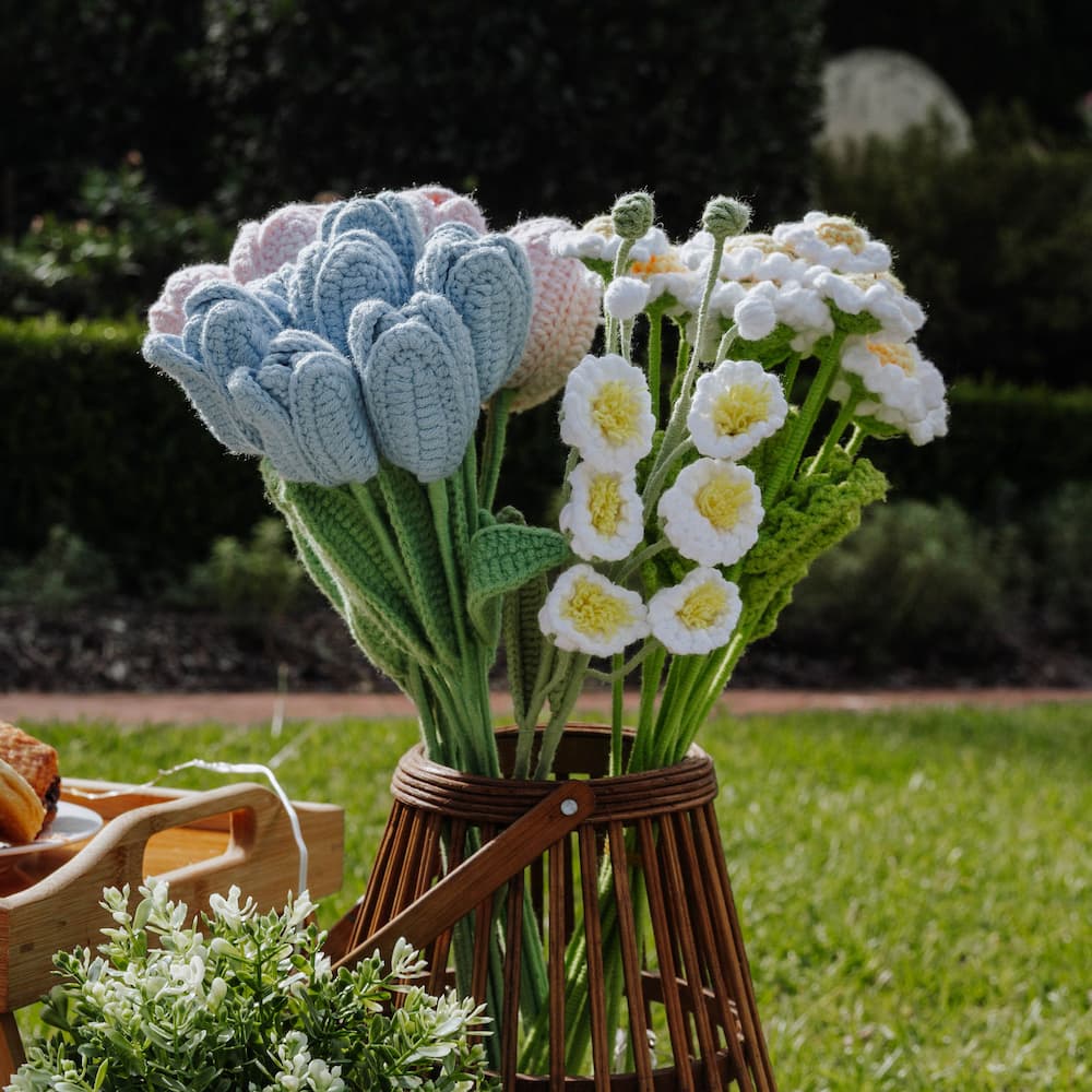 crochet flowers in a wooden basket on grass with blurred background