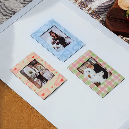 Three colorful magnetic photo frames on a white surface with a patterned rug and wooden object in the background.