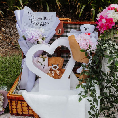 Valentine's Day gift basket with teddy bears, flowers, and a heart-shaped flower box outdoors.