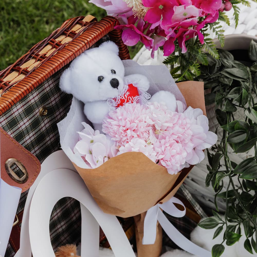White teddy bear with pink flowers in a wicker basket
