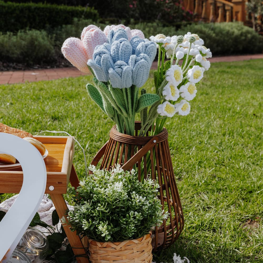 Decorative flowers in a woven vase on a grassy outdoor setting
