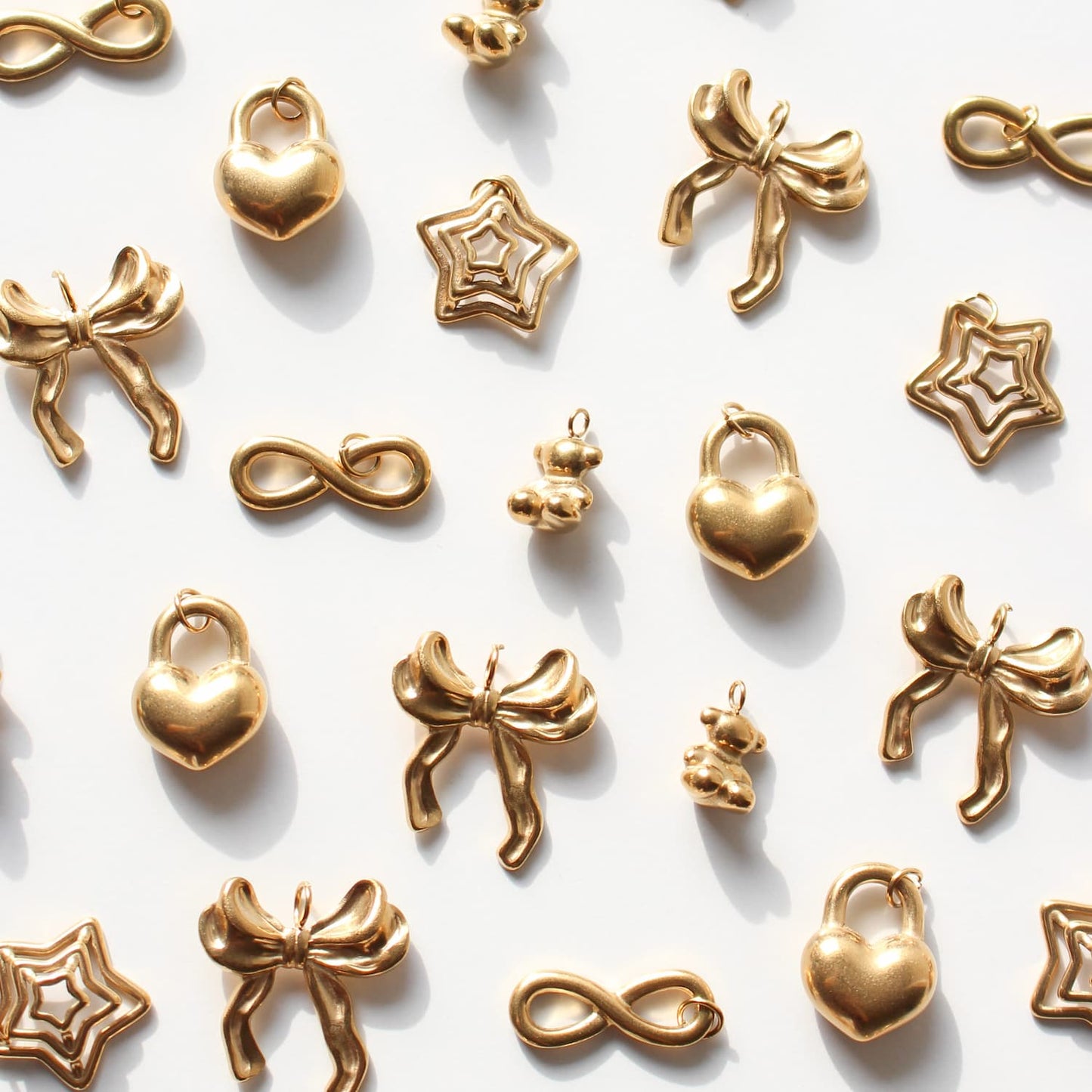 Gold jewelry charms including hearts, bows, and infinity symbols on a white background