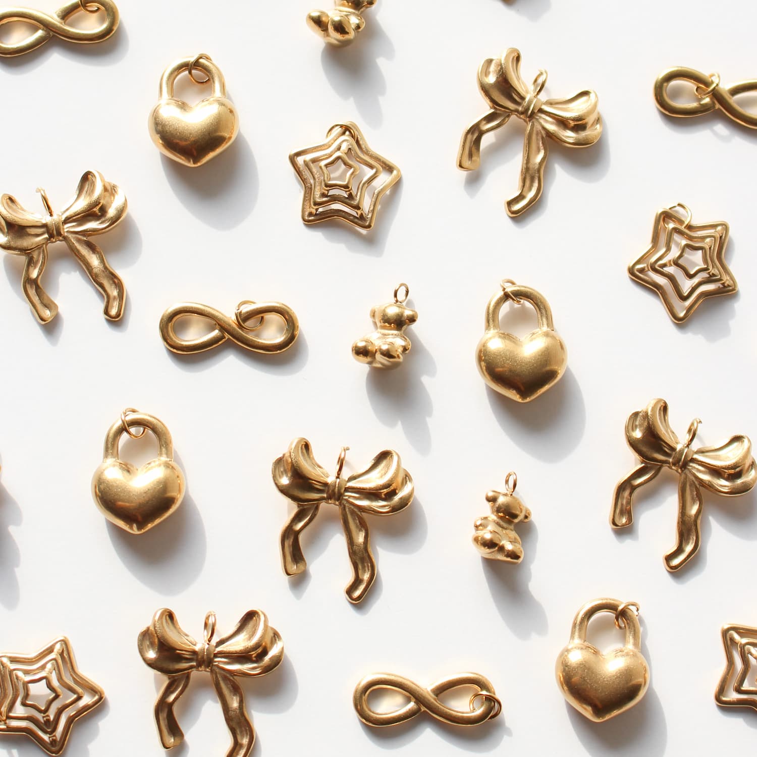 Gold jewelry charms including hearts, bows, and infinity symbols on a white background