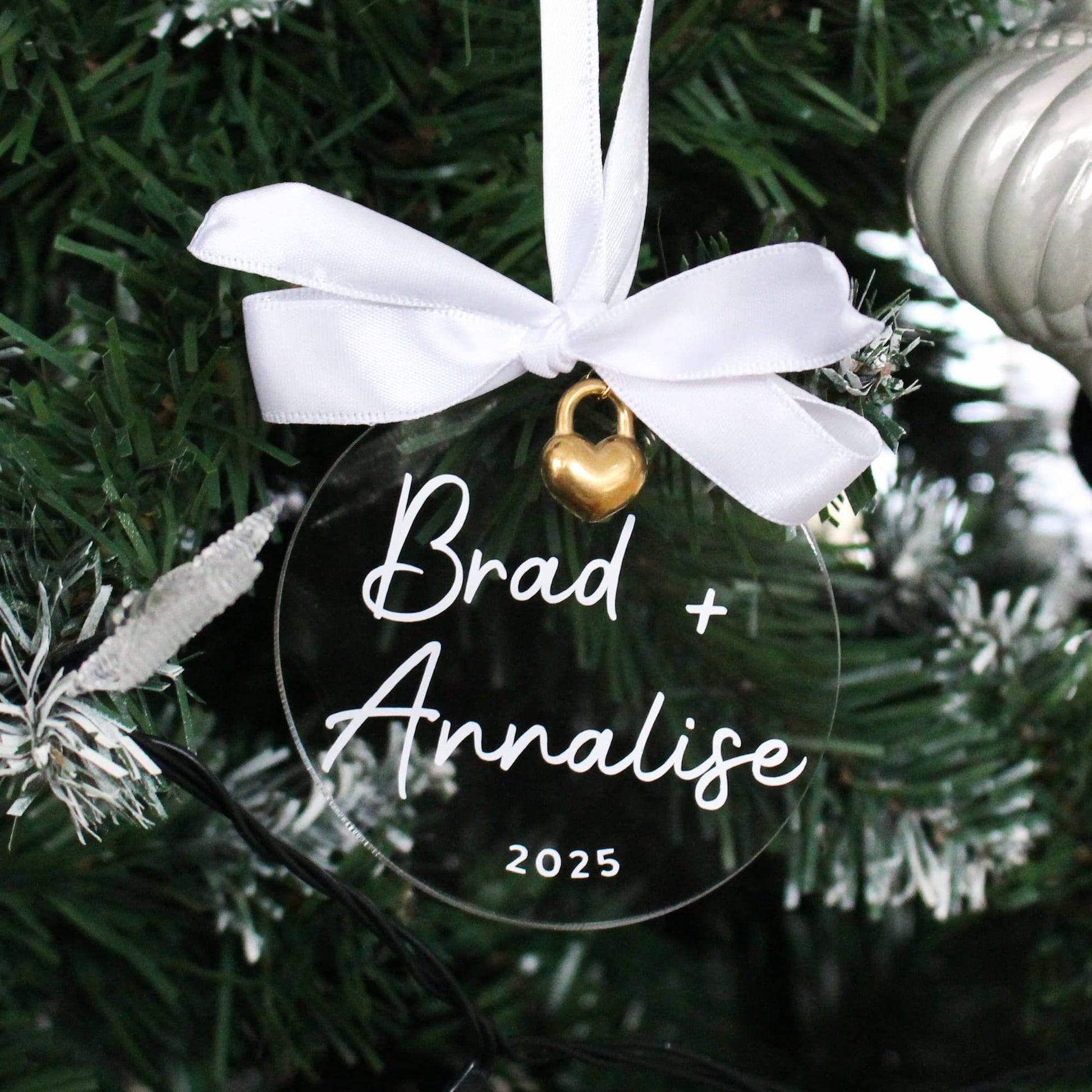 Personalised acrylic Christmas ornament with 'Brad + Analise 2025' text on a tree.