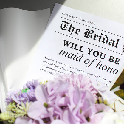 Newspaper with 'Will you be my maid of honor?' text and purple flowers.