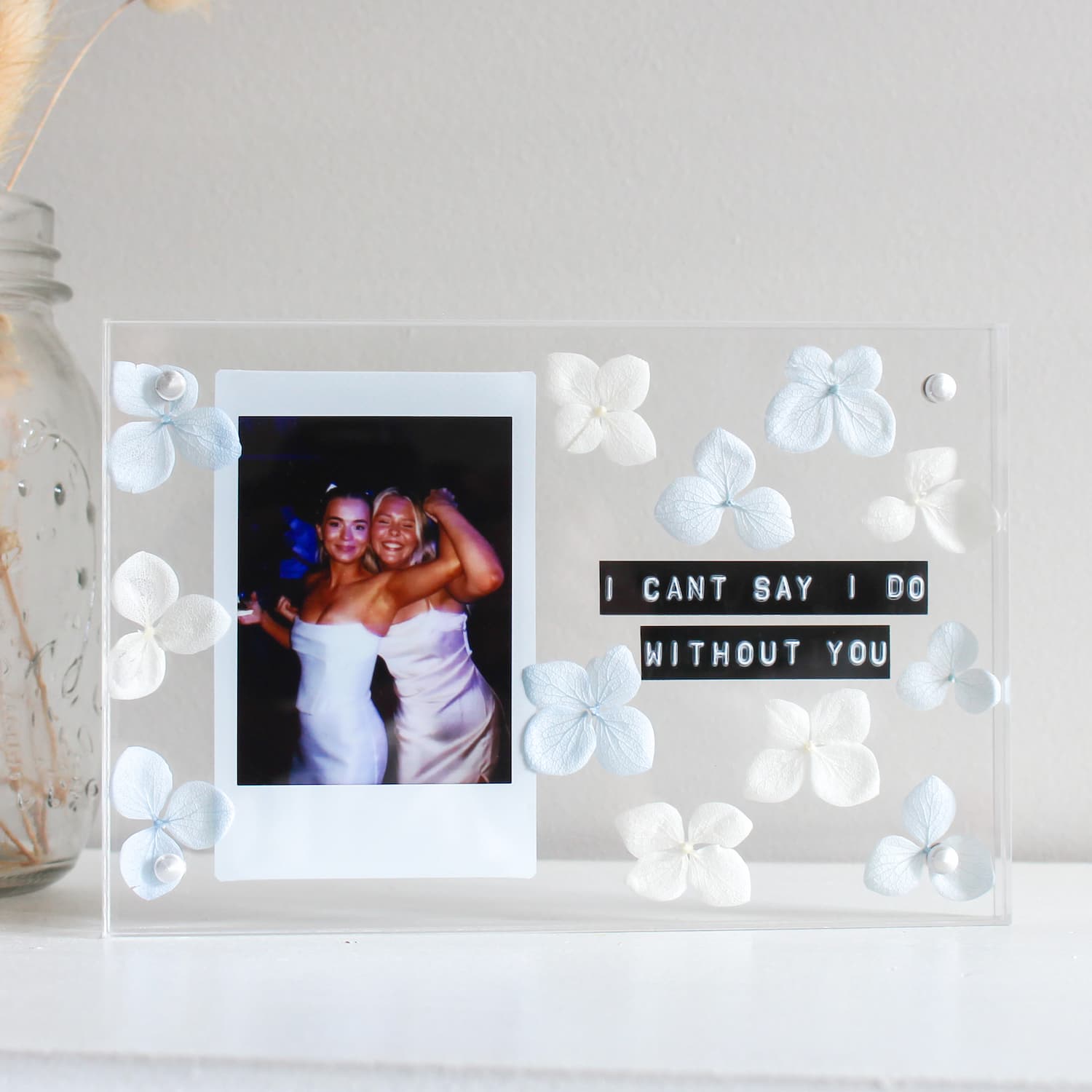 Decorative frame with a photo of two people and a message surrounded by white flowers on a light background.