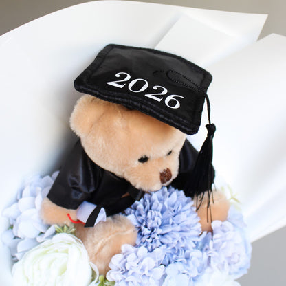 Teddy bear wearing a graduation cap with '2026' surrounded by flowers on a white background