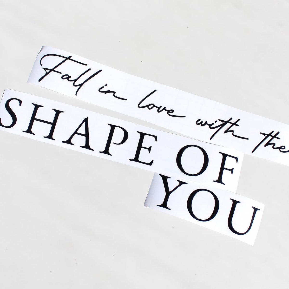 Two white rectangular decals with black text reading 'Fall in love with the SHAPE OF YOU' on a light gray background. personalised mirror decal