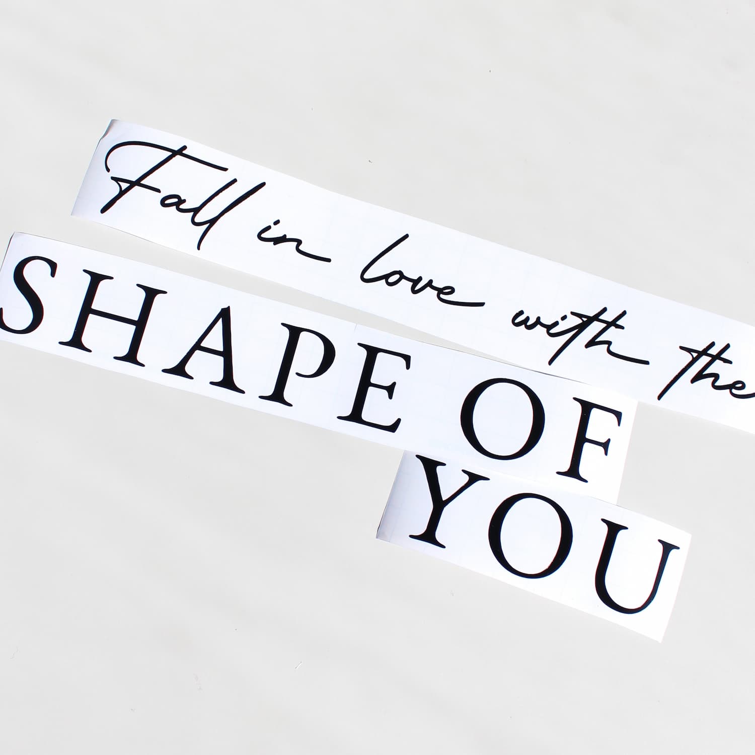 Two white rectangular decals with black text reading 'Fall in love with the SHAPE OF YOU' on a light gray background. personalised mirror decal
