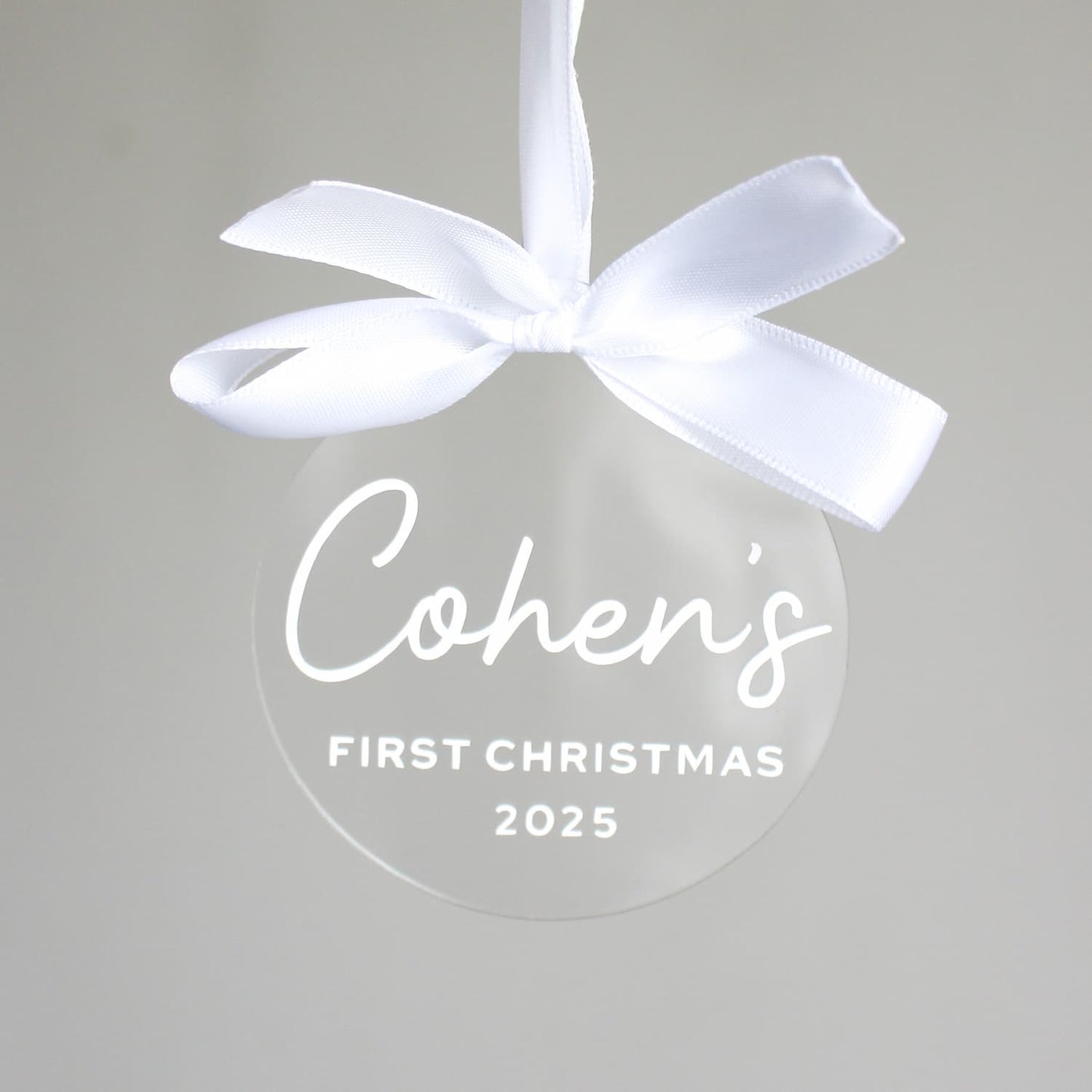 Clear ornament with white ribbon and 'Cohen's First Christmas 2025' text on a light gray background