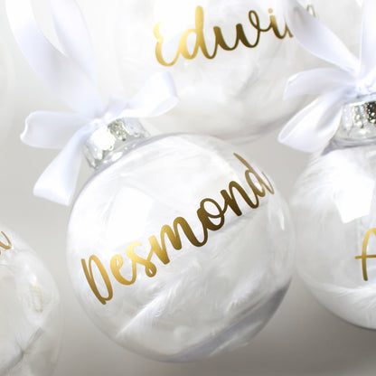 White ornaments with gold names and white ribbons on a light background