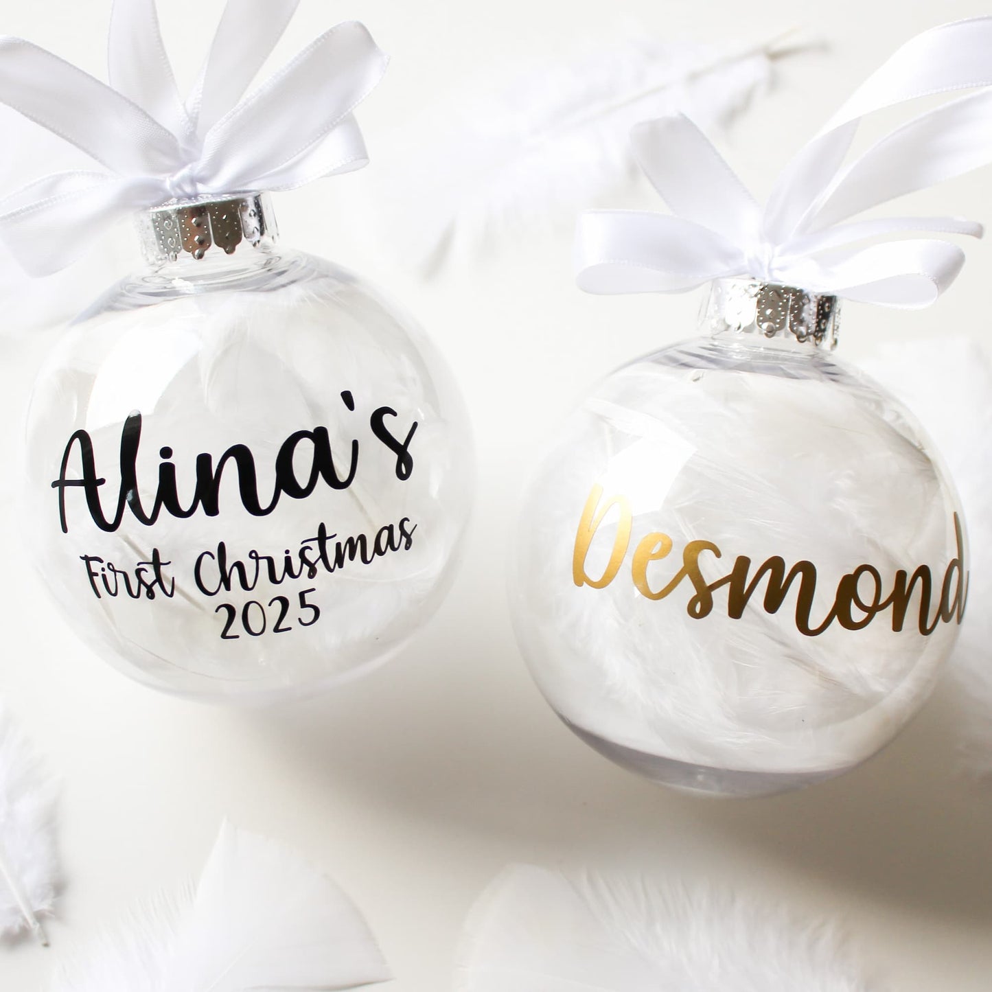 Two personalized Christmas feather ornaments with names and years on a white background