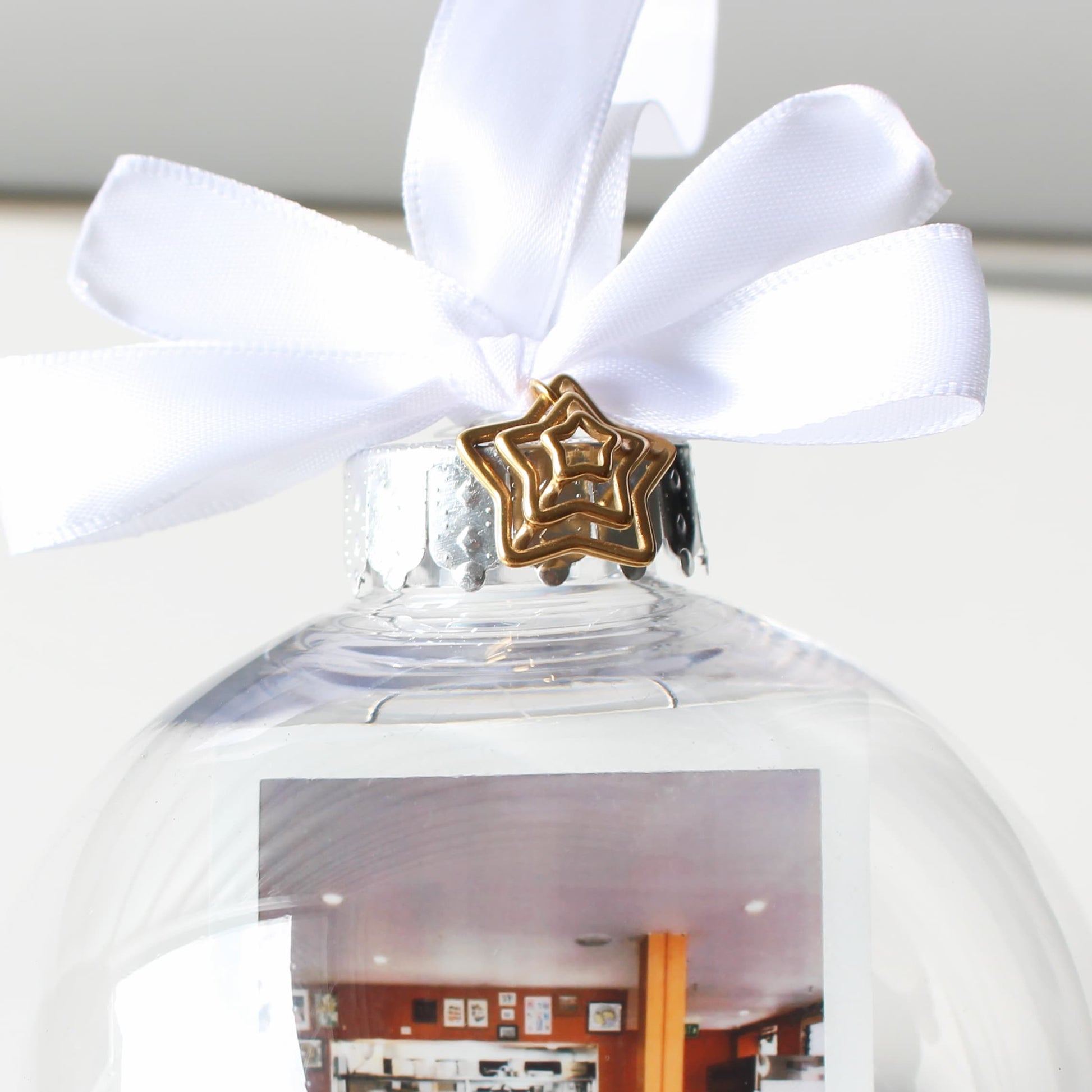 Clear glass ornament with a white ribbon and gold star-shaped charm, featuring a photo inside.