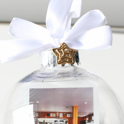 Clear glass ornament with a white ribbon and gold star-shaped charm, featuring a photo inside.